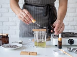 Woman pouring bulk fragrance oil in melt and pour candle wax, next to burner and lavender plants.