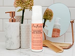SheaMoisture Curl Mousse bottle on white marble bathroom counter with white tiles and accessories.