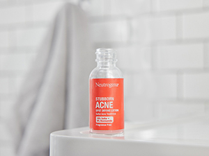 A hand holding a Glass bottle of Stubborn Acne Spot Drying Lotion