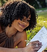 A beautiful woman with voluminous curly hair writing with a gold pen in her hair journal