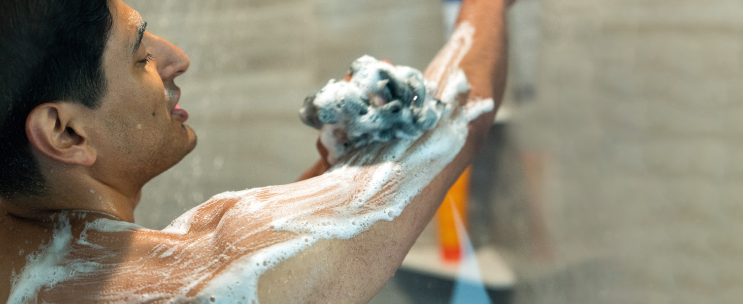 Man in shower with loofah bubbling and soaping his arm with Manodo Bourbon Leather bodywash