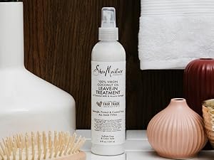 SheaMoisture leave-in treatment bottle on white counter with wooden background and bathroom items.