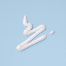 Beautifully spilled white lotion against pale blue background.
