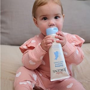 Baby sitting and holding bottle of Baby Jergens sensitive skin cream.