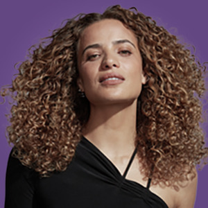 Woman with long, curly, healthy-looking hair posing on a purple  background. 