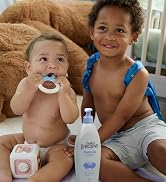 A baby sitting next to a toddler and a bottle of lotion