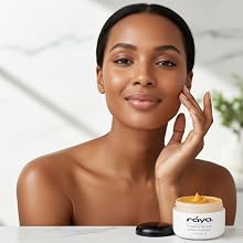 a black woman with a skin care product in front of her touches her face